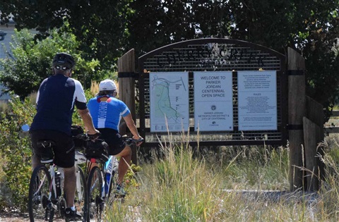 Cyclists riding past the Parker Jordan Centennial Open Space sign